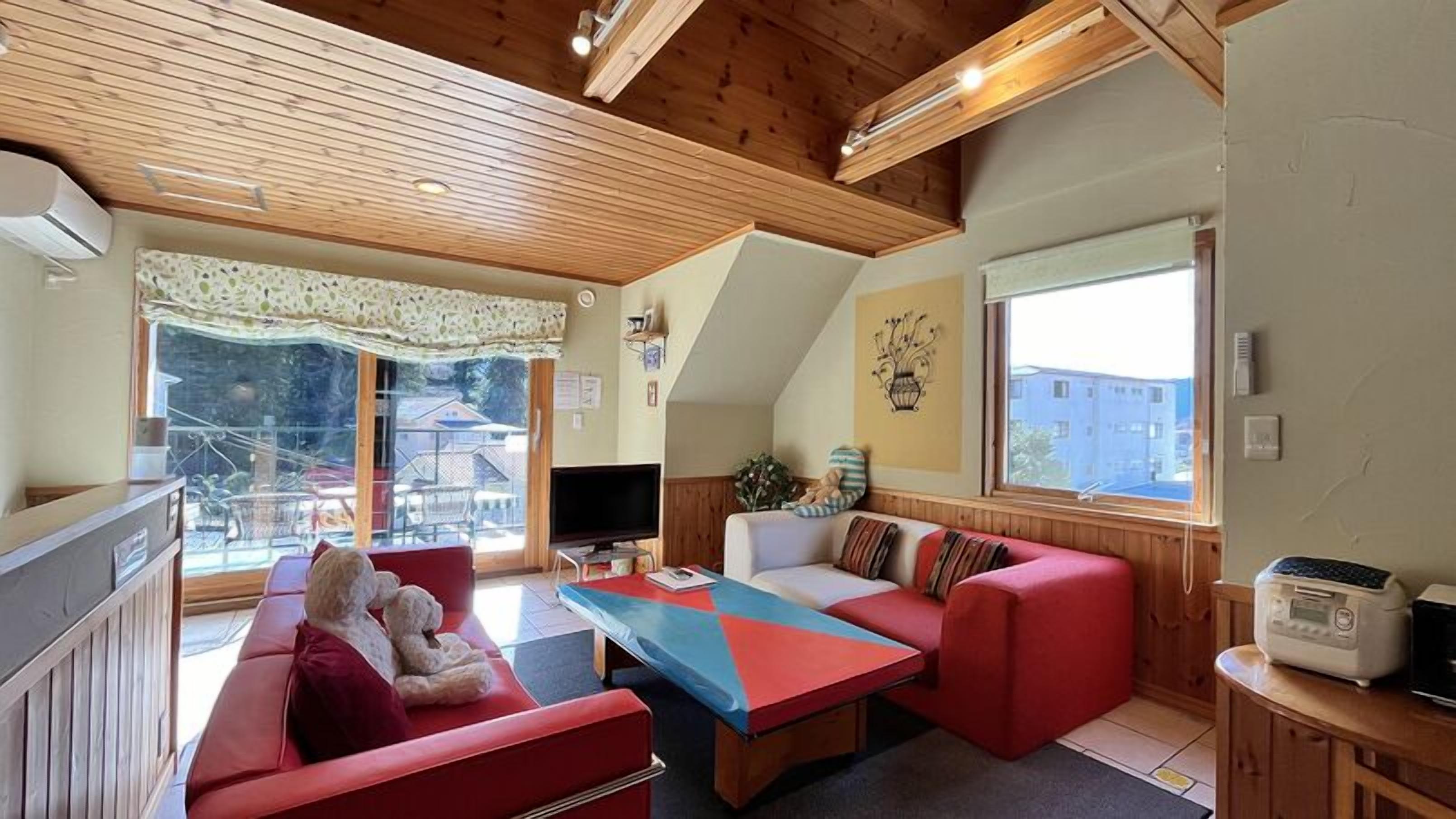 A cozy living room with a sofa, a coffee table, and a television. There is a window with a view of buildings outside.