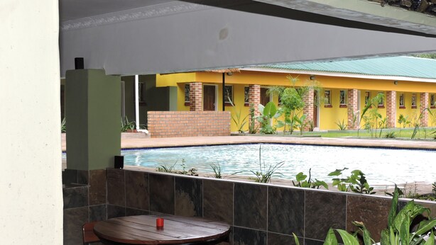 A poolside area with a table and chairs, surrounded by plants. - Café Zambezi House of Africa - Hostel (Livingstone)