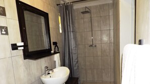 A bathroom with a white sink, a mirror, a shower, and a towel rack. - Café Zambezi House of Africa - Hostel (Livingstone)