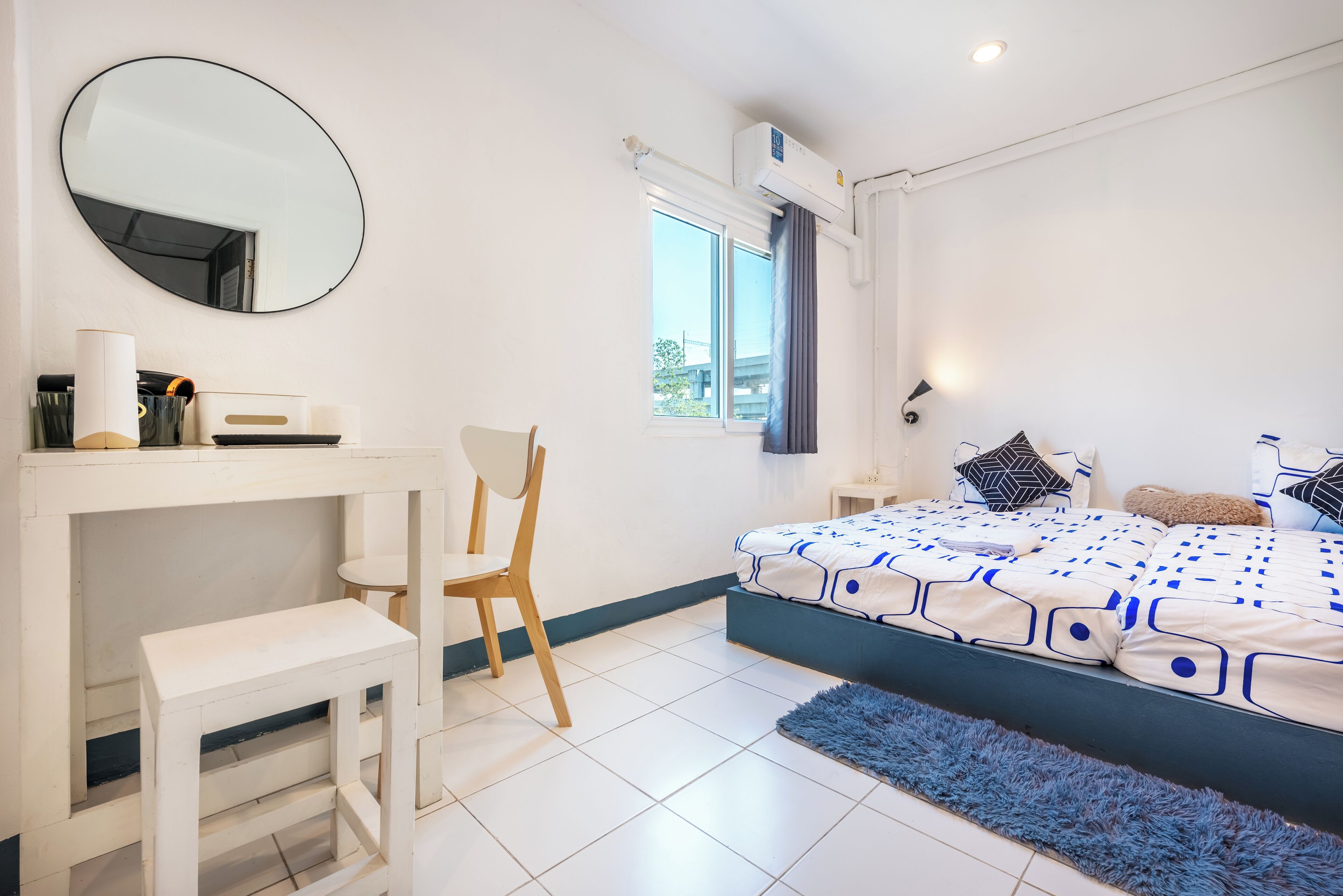 A bedroom with a bed, a desk, a chair, a mirror, and a window.