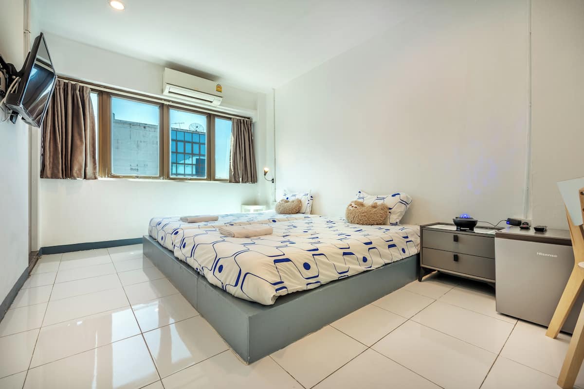 A modern bedroom with a large bed, a bedside table, a desk, and a television mounted on the wall.