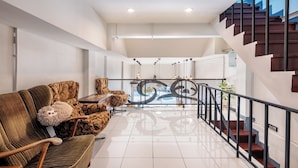 A spacious living area with a high ceiling, a staircase with a glass railing, and a view of the outside. - Sloth Hostel Don Mueang (Bangkok)