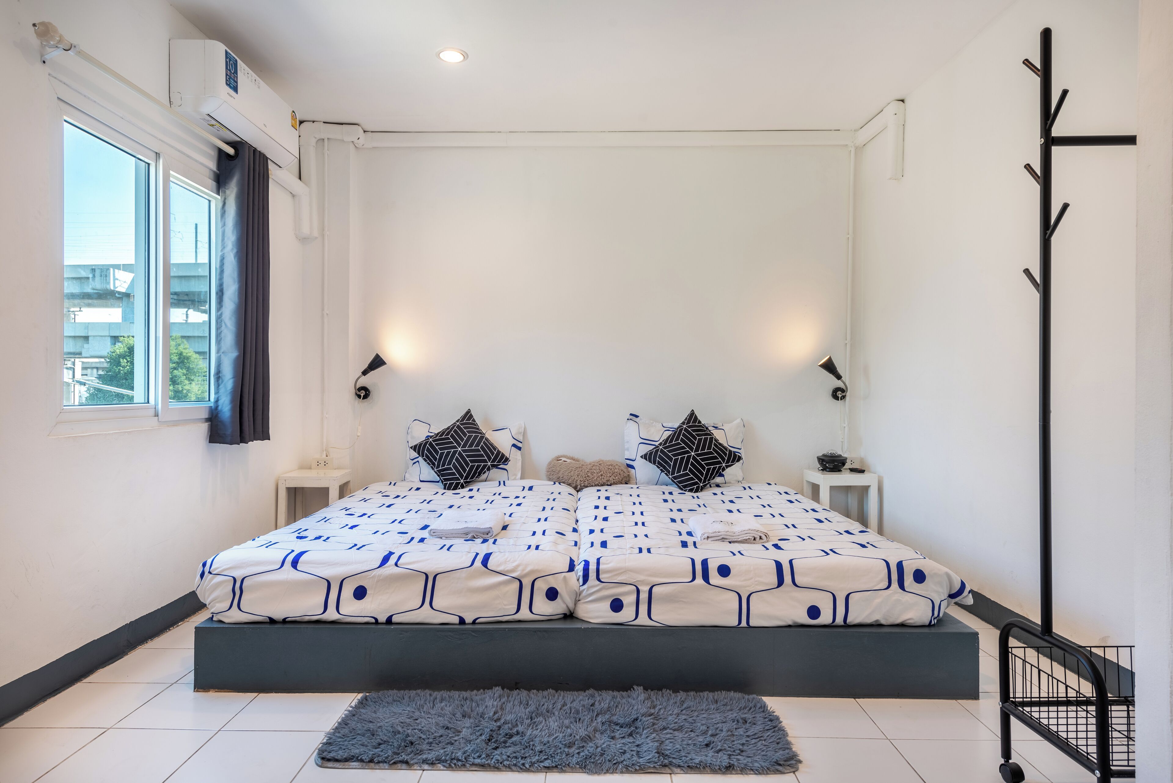 A modern bedroom with a large bed, two bedside tables, a black coat rack, and a window with curtains.