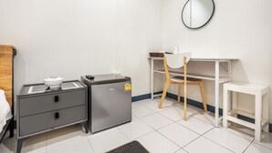 A compact hotel room with a bed, a small refrigerator, a desk with a chair, a white shelf, and a round mirror on the wall. - Sloth Hostel Don Mueang (Bangkok)