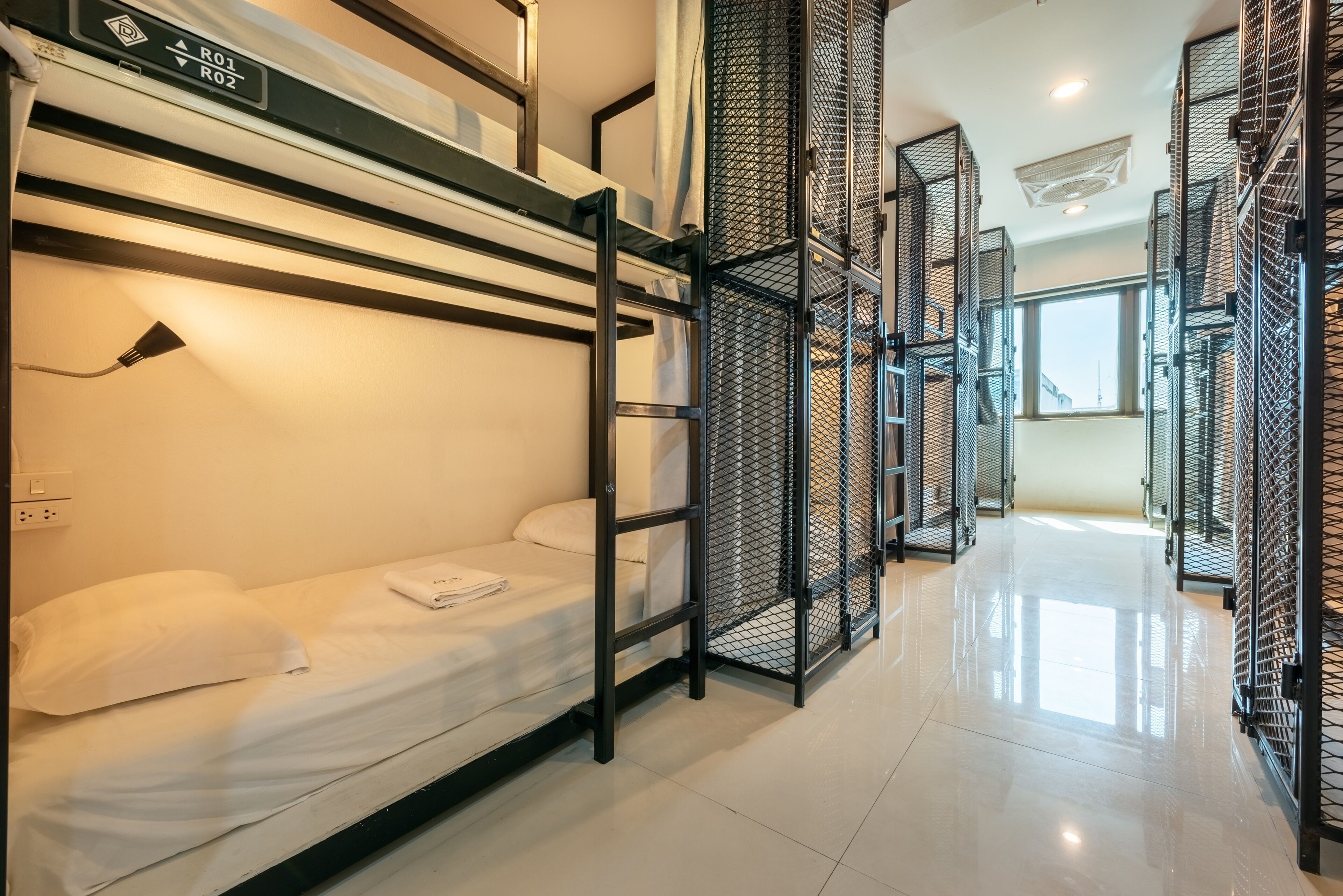 A modern hotel room with bunk beds, a metal partition, and a window providing natural light.