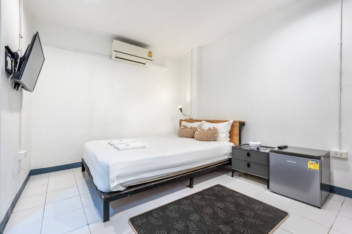 A bedroom with a bed, bedside table, a small desk, and a wall-mounted TV.