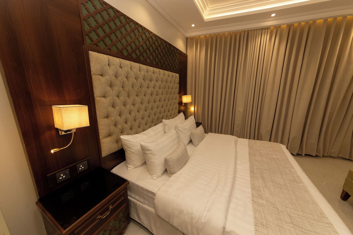 A hotel room with a large bed, a wooden headboard, a nightstand with a lamp, and a curtain.