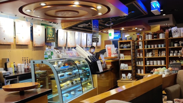 Un interno di un caffè con un bancone, una zona salotto e una vetrina con dolci.