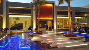 Un edificio moderno con area piscina, palme e persone nelle vicinanze.