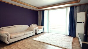 Una sala de estar con un sofá color beige, un tapete blanco y un ventanal corredero que da a un balcón.