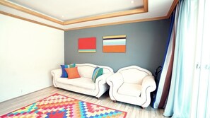 A living room with two white sofas, colorful cushions, a patterned rug, and two abstract paintings on the wall.