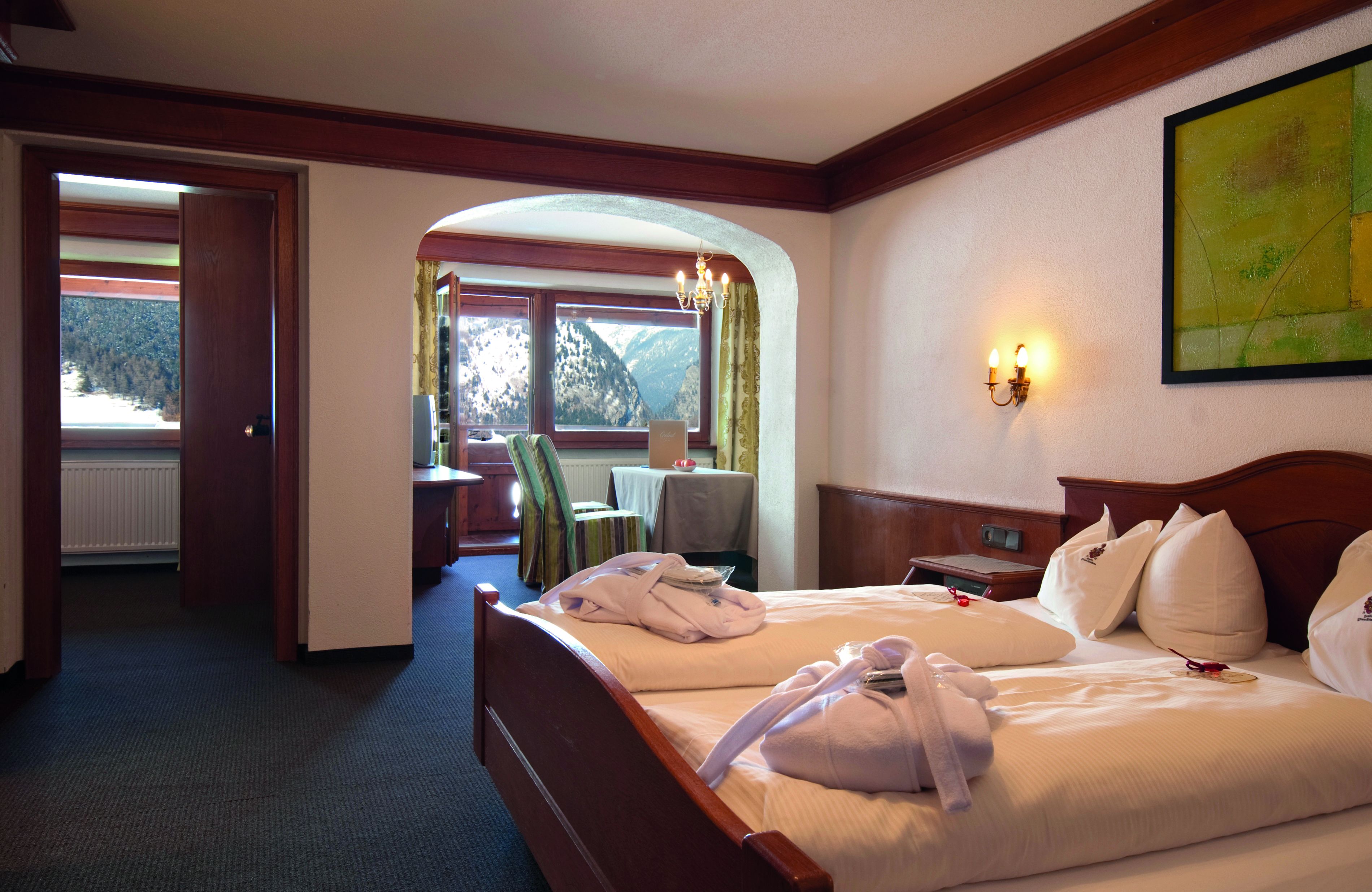 A hotel room with a bed, a desk, a chair, and a view of mountains through a window.