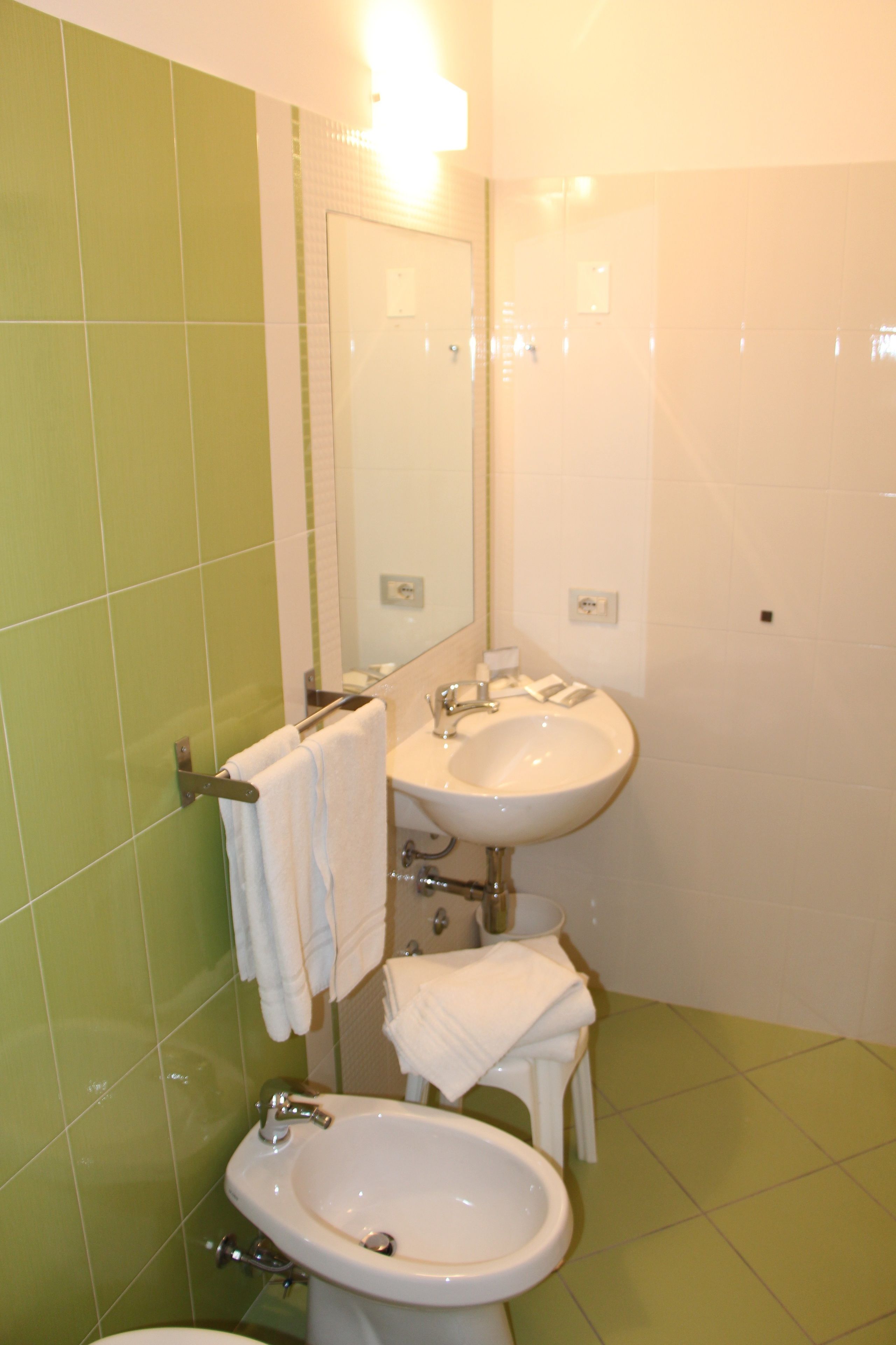 Un baño con azulejos verdes, un lavamanos, un bidé y un espejo.
