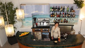 A bar area with a curved counter, a variety of bottles and glasses, and a tiled backsplash. - Hotel Confort (Cattolica)