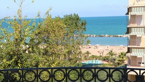Un hotel frente a la playa con piscina, vista al mar y balcón con barandilla.