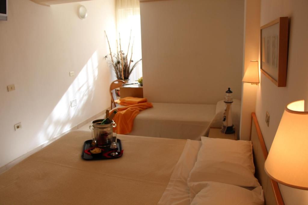Habitación de hotel con dos camas, una mesita de noche con lámpara, una pequeña mesa con una botella y vasos, y un ventanal con cortinas.