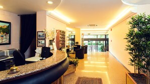 Zona de recepción de hotel con un mostrador curvo, asientos, un escritorio de recepción, una computadora y una planta en maceta.