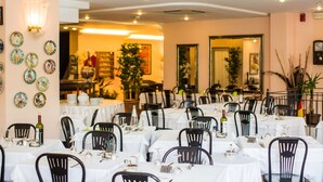 Un restaurante con mesas redondas, sillas negras y manteles blancos.
