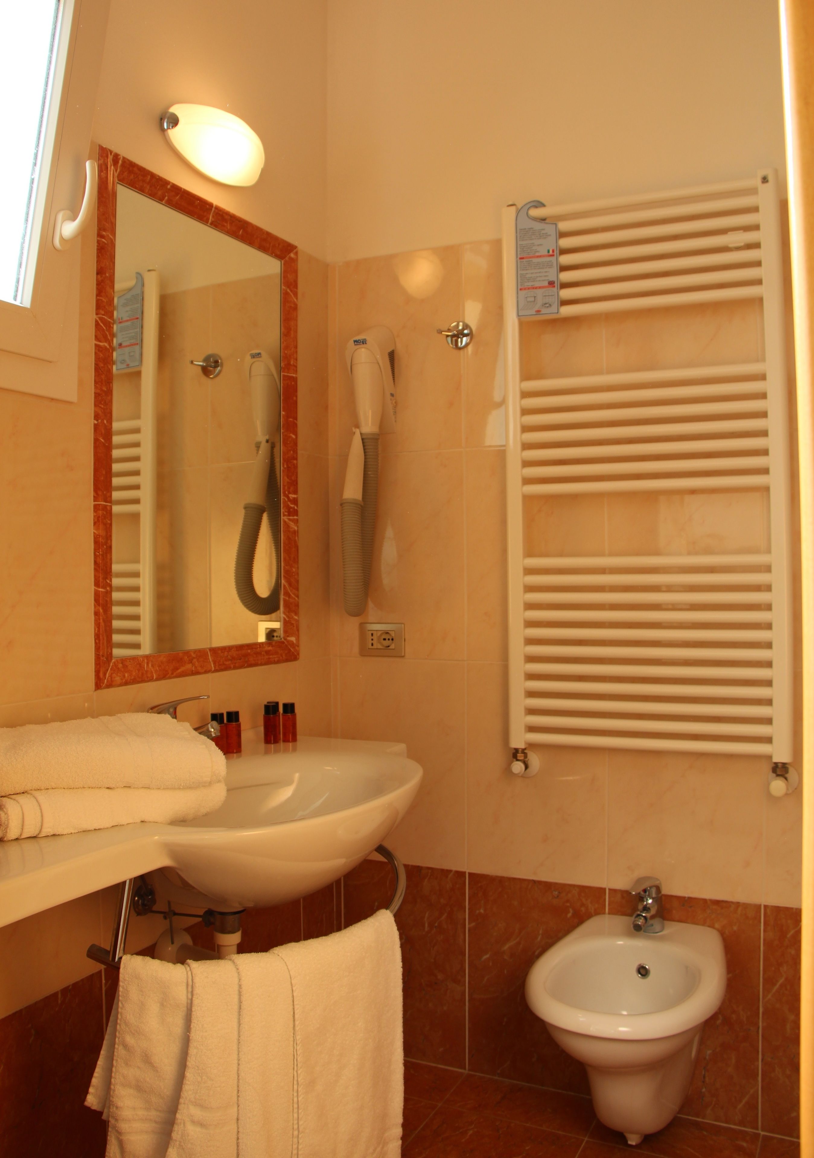 Et badeværelse med håndvask, bidet, håndklædestige og et spejl.