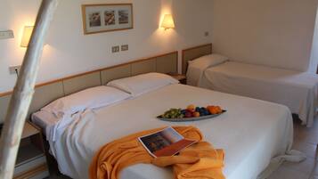 A hotel room with two beds, a bedside table with a fruit bowl, and a lamp on the wall.