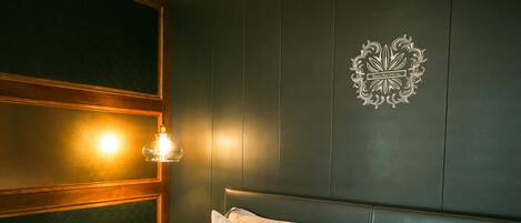 Una habitación de hotel con una cama, una mesita de noche, un aplique de pared y un emblema decorativo.