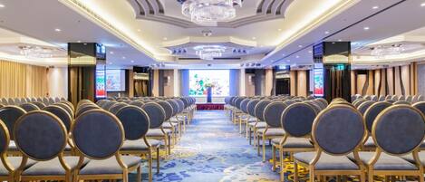 Un salón de conferencias con filas de sillas, piso alfombrado y un candelabro.