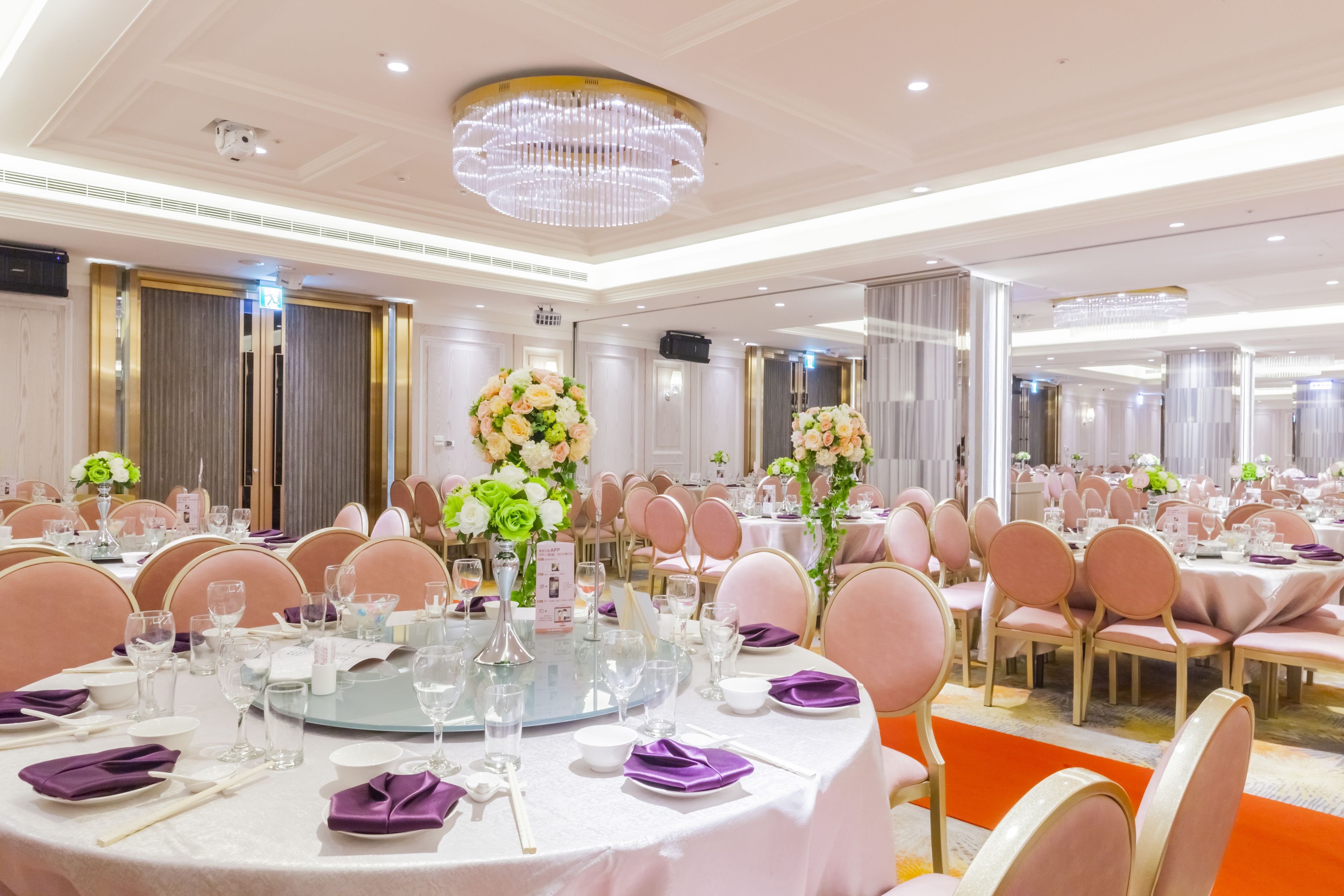 A banquet hall with round tables, pink chairs, and floral centerpieces.