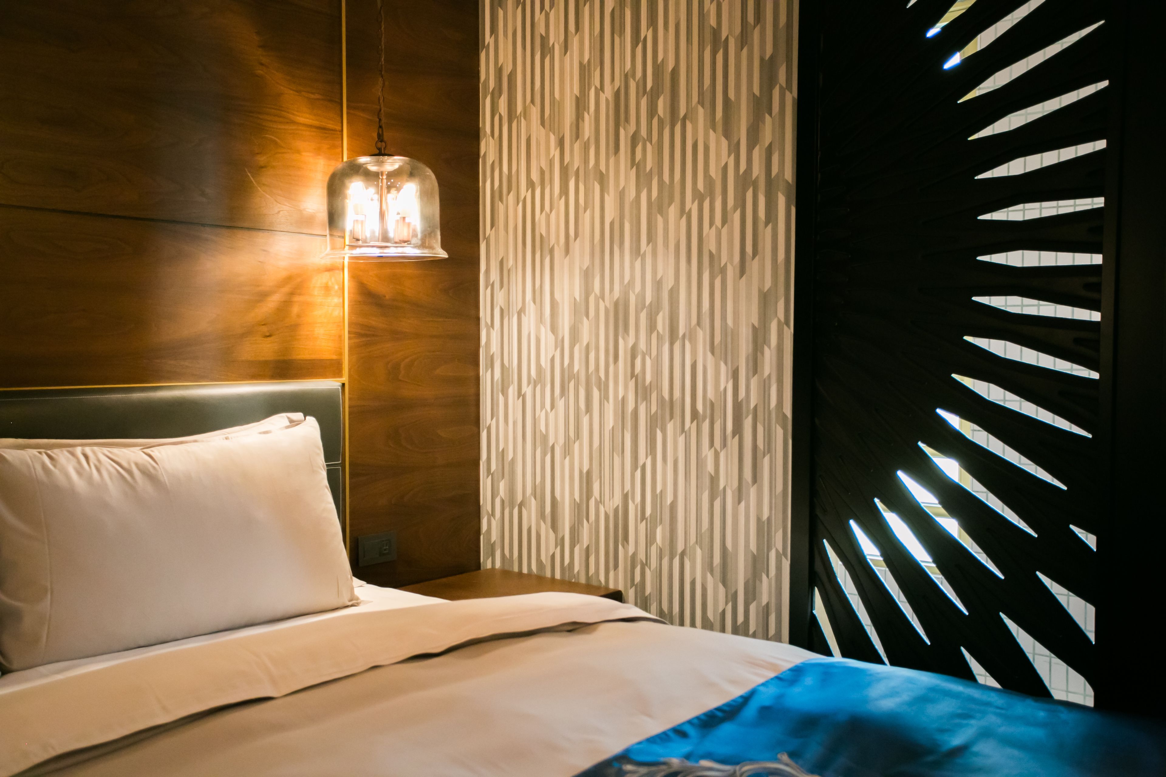 A modern hotel room with a wooden headboard, a patterned wall, and a geometric window design.
