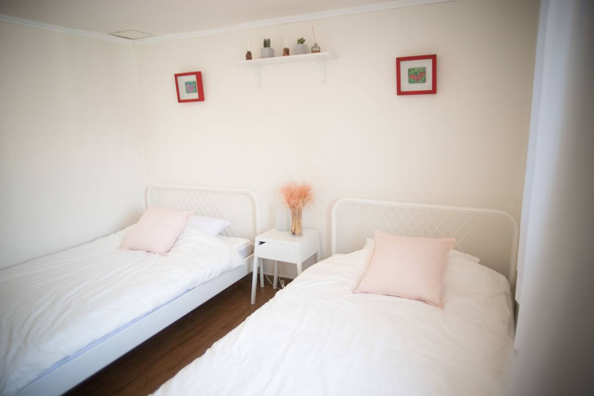 A twin room with two single beds, a small bedside table with a vase, and a shelf above the beds.