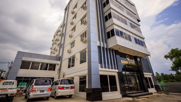 A multi-story hotel with a modern design, featuring a prominent entrance and several parked vehicles in front. - Seoul Hotel Myanmar (Yangon)