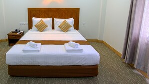 A hotel room with a large bed, two bedside tables, a nightstand, and a wall-mounted light. - Seoul Hotel Myanmar (Yangon)
