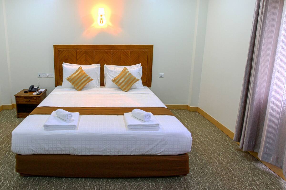 A hotel room with a large bed, two bedside tables, a nightstand, and a wall-mounted light.