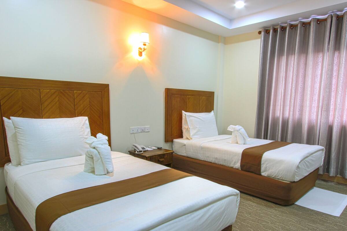 A hotel room with two beds, a bedside telephone, a wall-mounted light, and a window with curtains.
