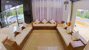 A modern hotel lobby with a large seating area, a large window with a view of parked cars, and an air conditioning unit. - Seoul Hotel Myanmar (Yangon)