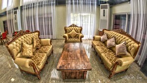 A formal sitting room with two ornate sofas and a central coffee table, featuring a high ceiling and large windows with sheer curtains. - Seoul Hotel Myanmar (Yangon)