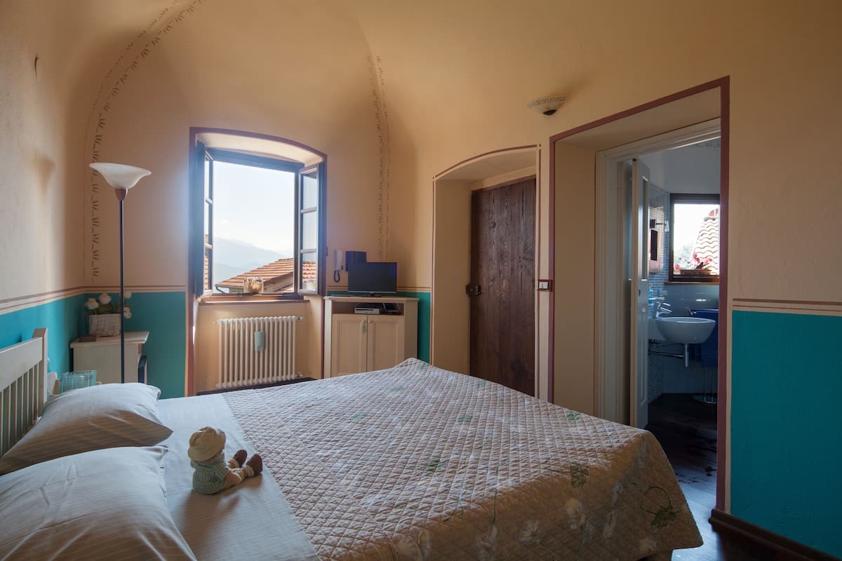 A bedroom with a bed, a nightstand, a lamp, a dresser, and a window.