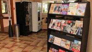 Un área de recepción con un atril para revistas, una máquina expendedora y un basurero.