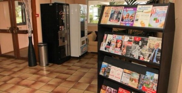A reception area with a magazine rack, a vending machine, and a trash bin. - Hotel Motelia (Moissy-Cramayel)
