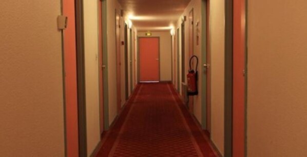 A long, narrow hallway with doors on both sides and a red carpet. - Hotel Motelia (Moissy-Cramayel)