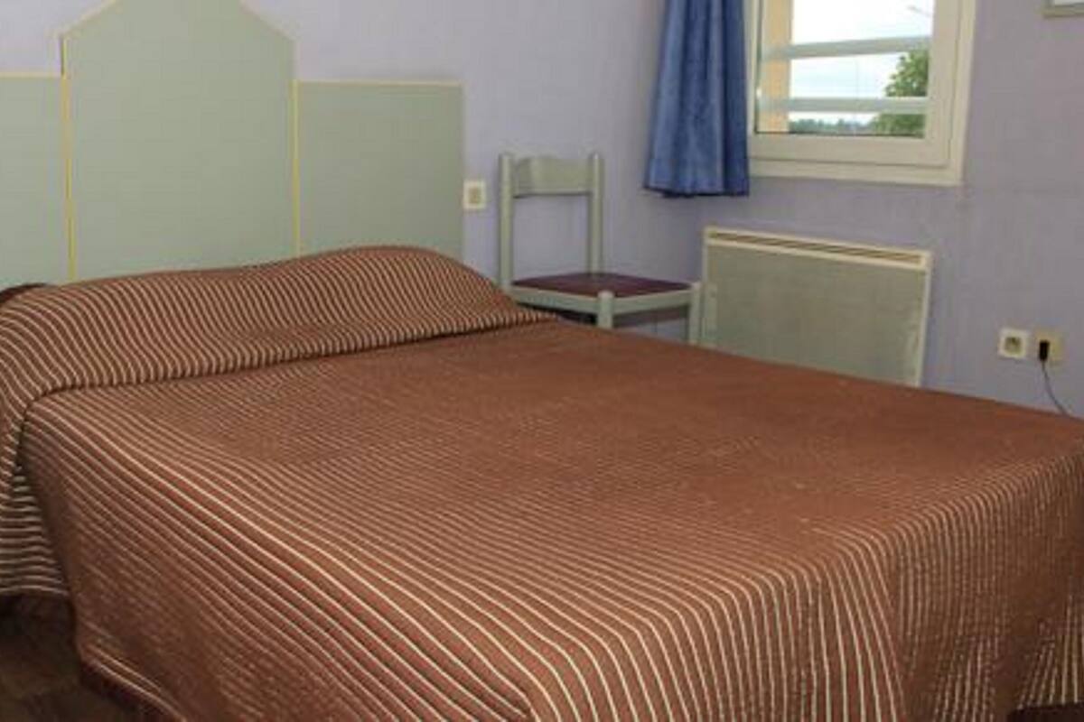 A bedroom with a bed, a chair, a radiator, and a window with curtains.