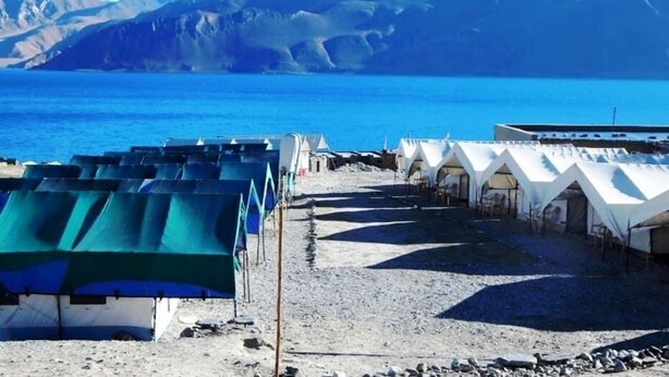 A coastal area with tents and a building, likely a campsite or temporary accommodation, with a clear view of the sea and mountains in the background. - Wonderland Camps (Leh)