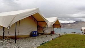 Three tents set up on a gravel area with a lake and mountains in the background. - Wonderland Camps (Leh)