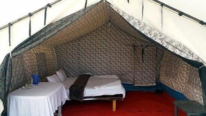A tented accommodation with a single bed, a small table with a chair, and a red carpeted floor. - Wonderland Camps (Leh)