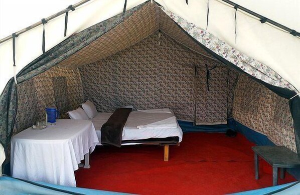 A tented accommodation with a single bed, a small table with a chair, and a red carpeted floor.