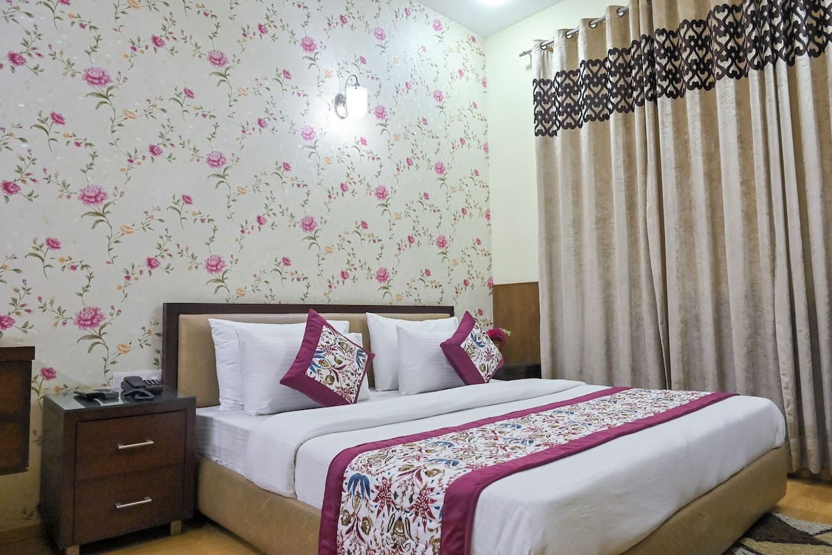 Un lit bien fait, recouvert d’une couvre-lit à motifs floraux et agrémenté d’oreillers, une table de chevet avec un téléphone et une télécommande, et un mur recouvert d’un papier peint à fleurs.