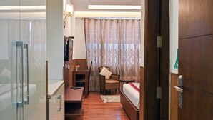 A hotel room with a wooden floor, a bed, a desk, a chair, a small table, and a glass partition. - Imperial Apartments Gurugram (Gurugram)