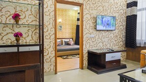 A hotel room with a bed, a TV, a wooden desk, and a glass cabinet with vases. - Imperial Apartments Gurugram (Gurugram)