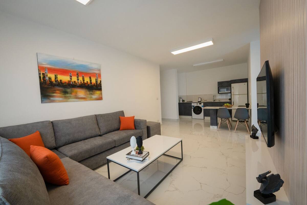A modern living room with a grey sofa, a coffee table, and a painting of a cityscape.