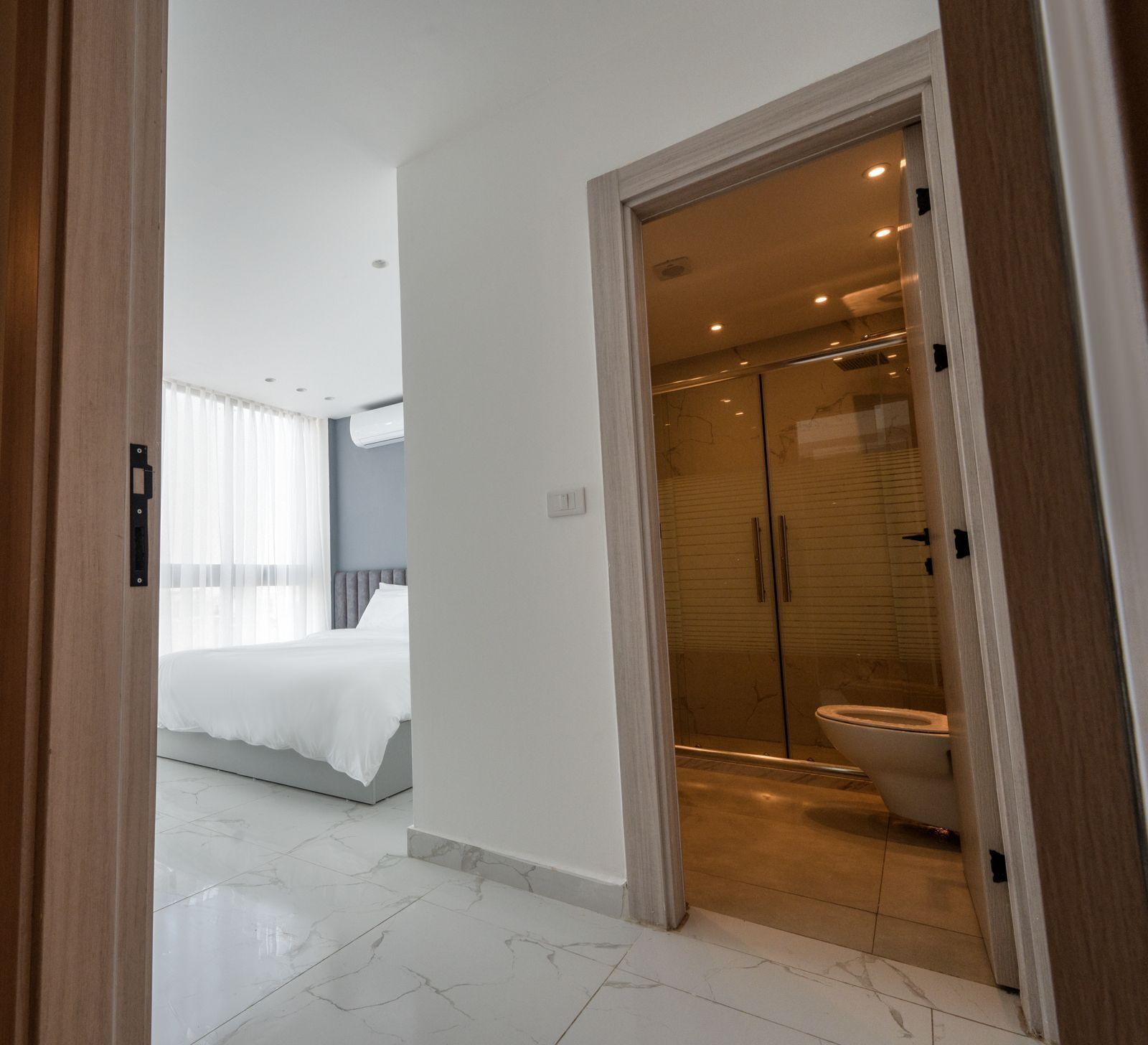 Un dormitorio moderno con una cama grande, un baño con cabina de ducha de vidrio y un pasillo.