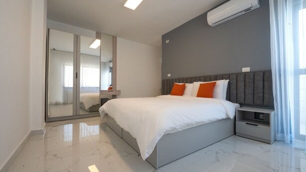 A modern bedroom with a large bed, a nightstand, a mirror, and an air conditioning unit.